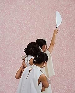 Three women in white sleeveless tops holding a curved blade against pink floral wallpaper