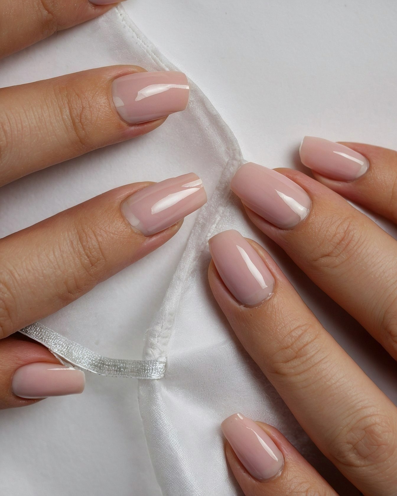 Close-up of milky pink nails on white fabric