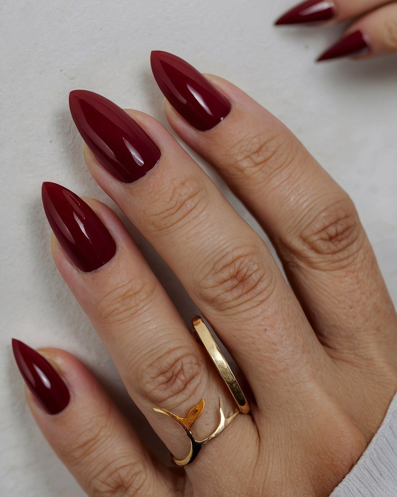 Close-up of deep crimson nails with gold ring