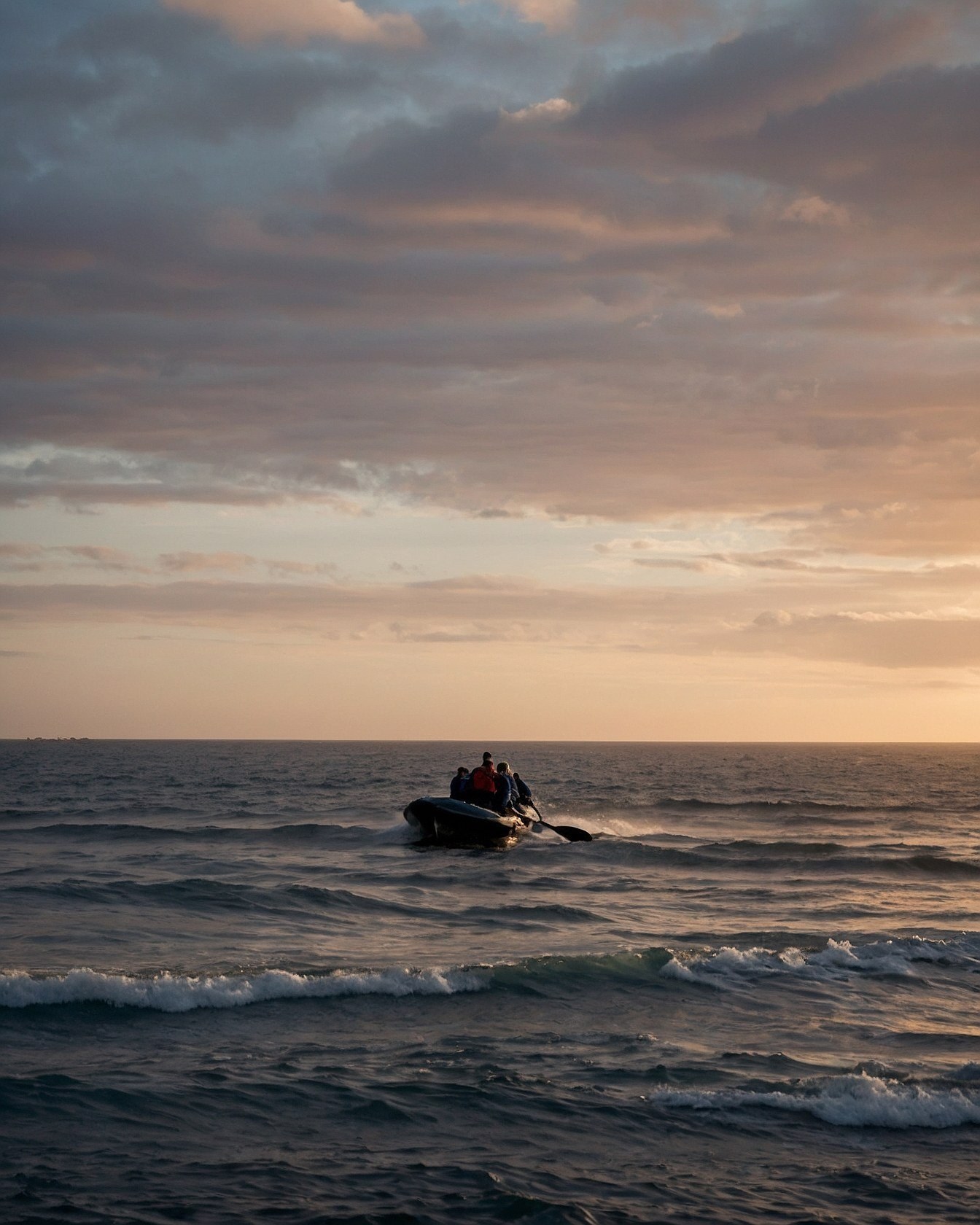 Inflatable boat cuts through dusky ocean waves