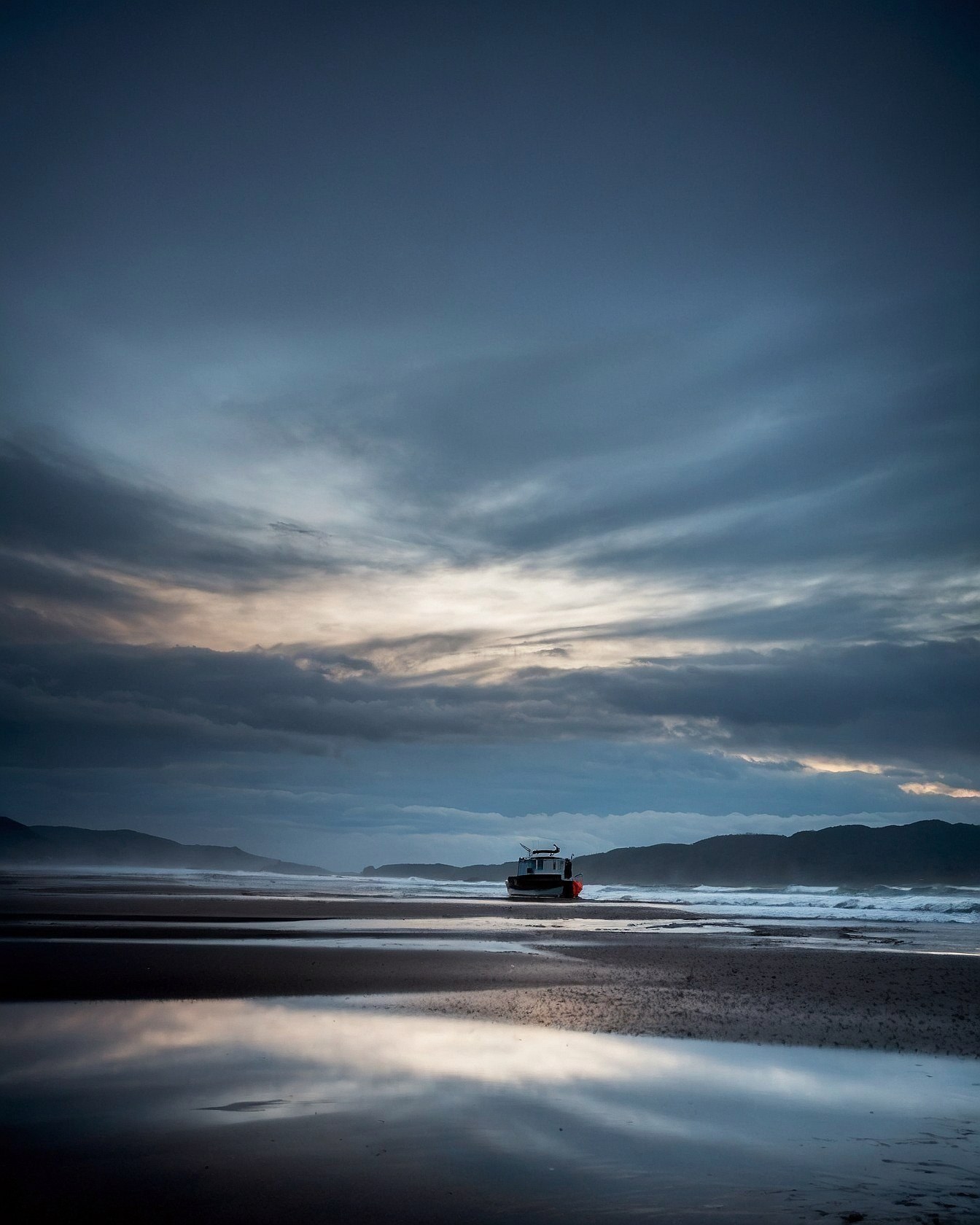 A solitary fishing boat resting on wet sand beneath a sprawling azure sky