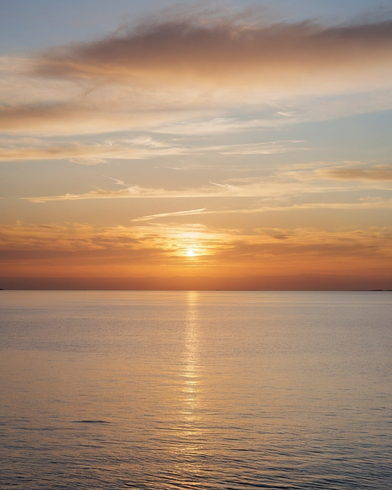 Muted slate grey sea beneath a glowing amber sunset horizon