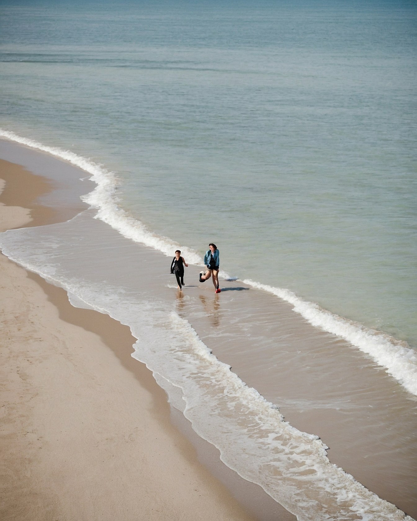 Two figures striding into the ocean surf